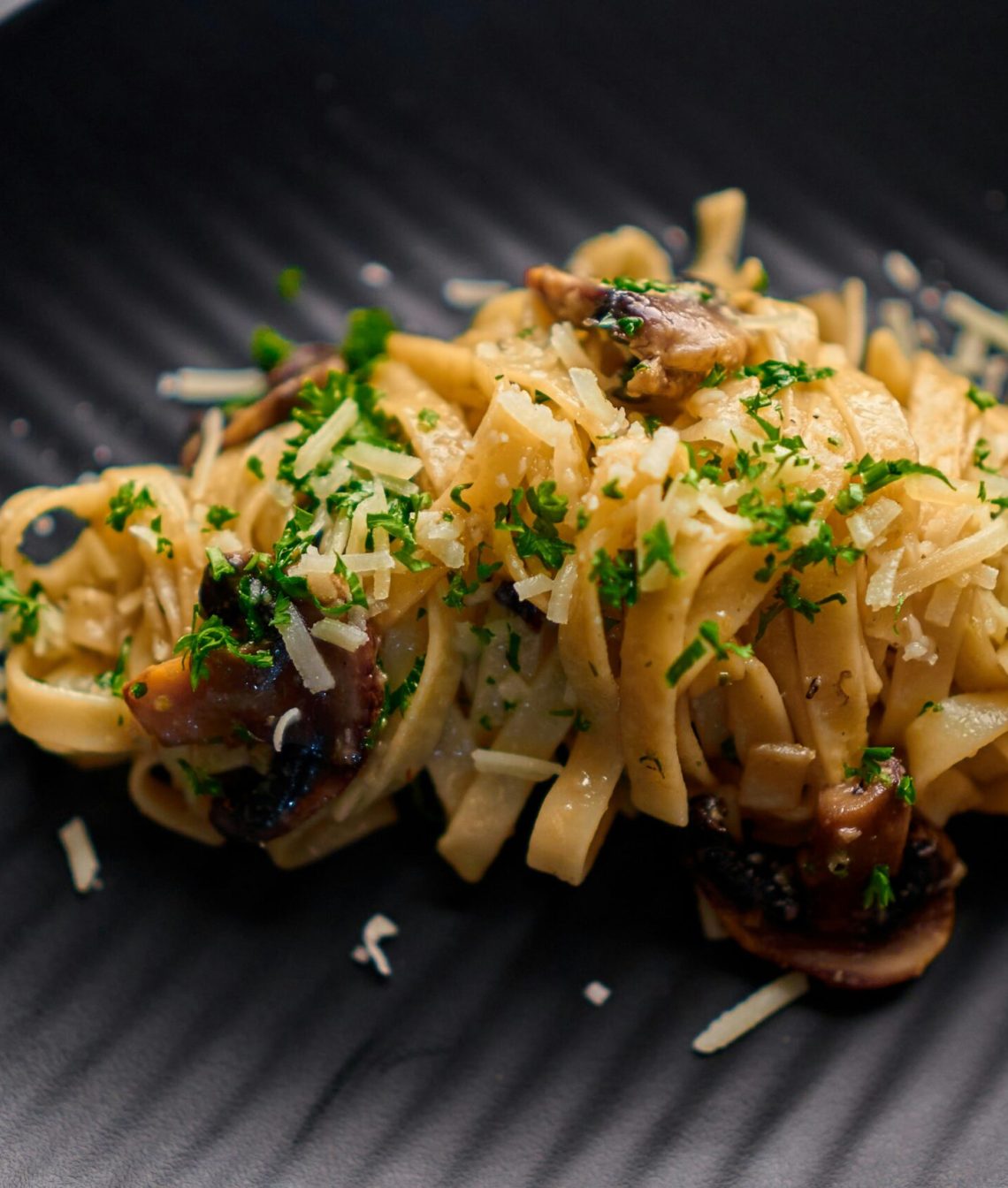 Pasta mit Champignons und Käse auf einem schwarzen Teller
